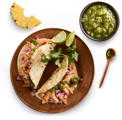 A wooden plate featuring chicken tacos topped with cilantro, lime, onion and pineapple.