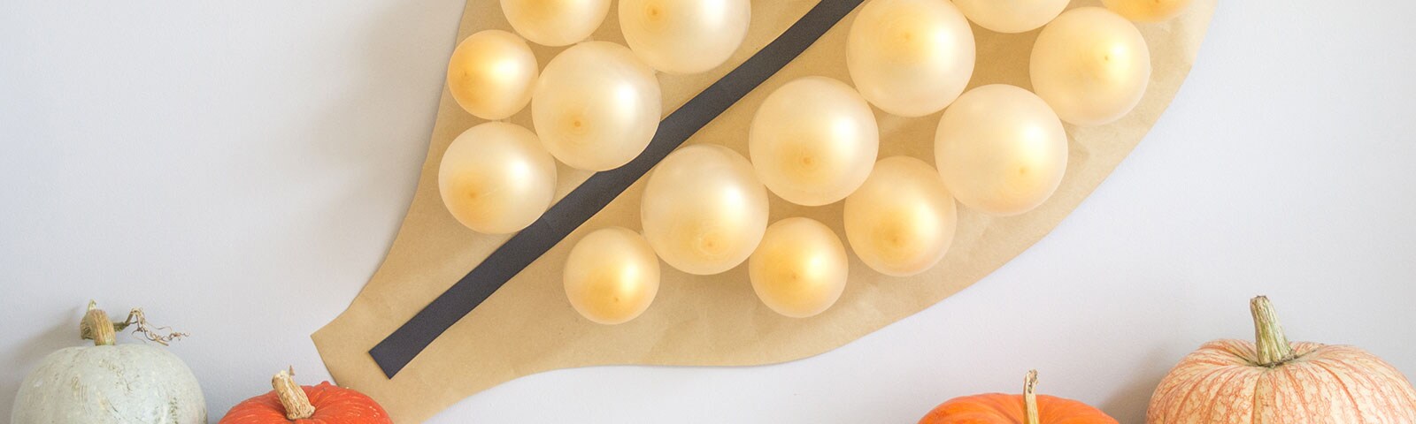 Several confetti-filled balloons attached to a leaf-shaped piece of brown craft paper surrounded by small pumpkins