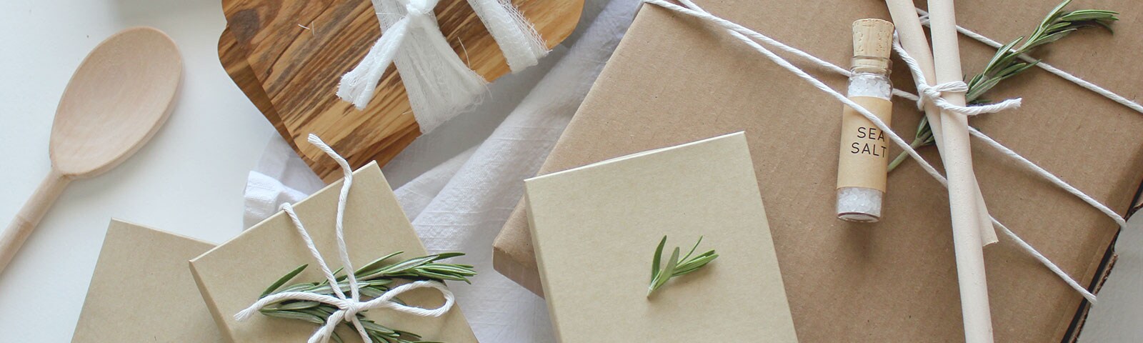 Wooden spoons, a vial of sea salt, cardboard, twine, rosemary and a cutting board wrapped in cheesecloth laid out on a white table Wooden spoons, a vial of sea salt, cardboard, twine, rosemary and a cutting board wrapped in cheesecloth laid out on a white table
