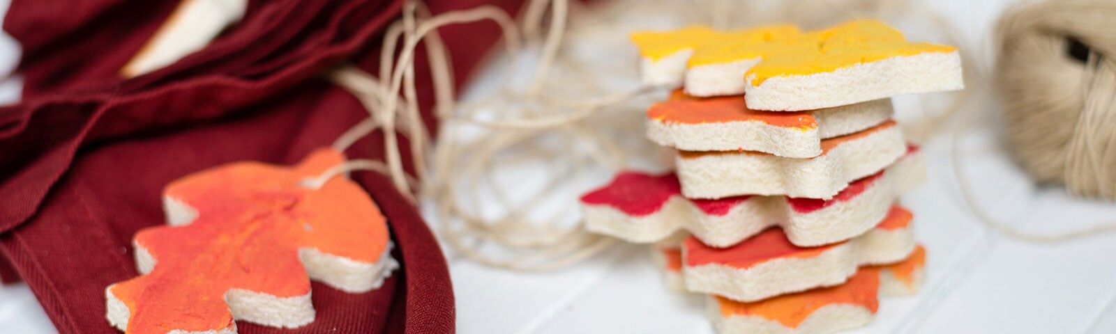 Homemade ornaments on a white table in the shape of leaves painted different shades of red, orange and yellow.