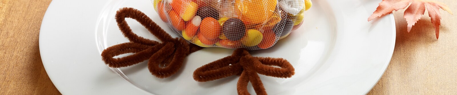 A bag of mixed candy with turkey legs made from brown pipe cleaners sit on a white plate