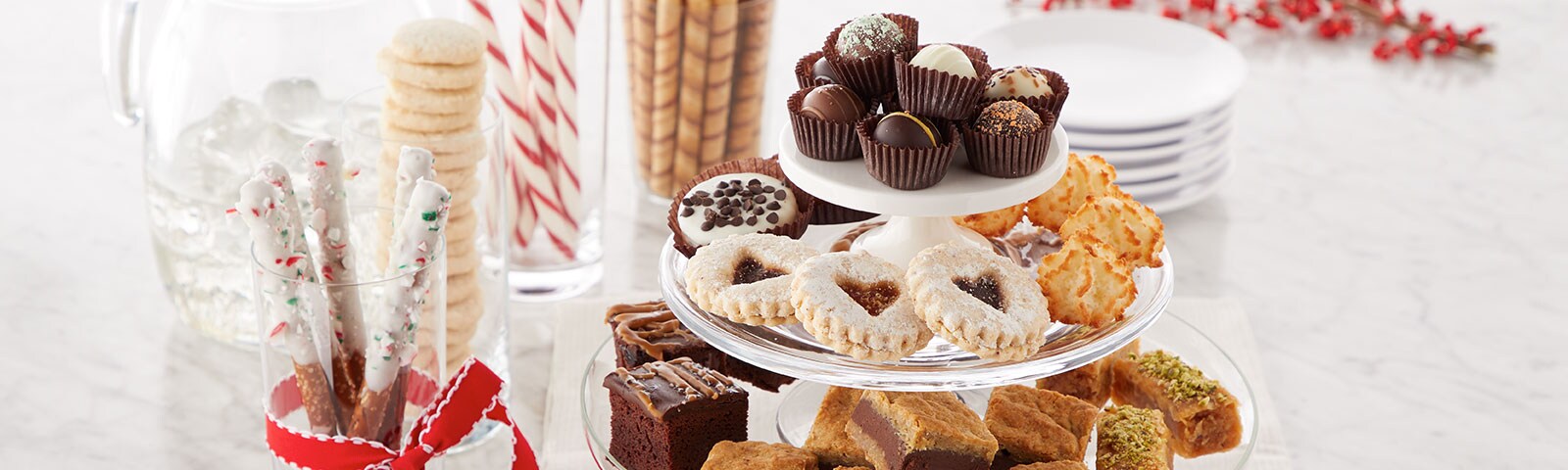 A cake platter filled with pastries on a table next to chocolate-dipped pretzel sticks and other treats in jars or vases