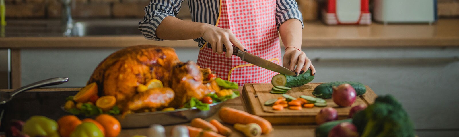 A person chops a cucumber while a cooked turkey sits in a pan in the foreground